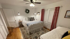 Ein Schlafzimmer mit Bett, Deckenventilator, Teppich und einem Fenster mit Vorhängen.
