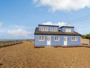 A two-story house with a blue exterior and white trim, located on a gravel driveway with a wooden fence in the background. - 4 bedroom accommodation in Reighton Gap, near Filey (Reighton Gap, near Filey)