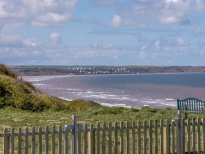 A coastal view with a wooden fence and a bench, overlooking a beach and buildings in the distance. - 4 bedroom accommodation in Reighton Gap, near Filey (Reighton Gap, near Filey)