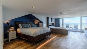 Une chambre moderne avec un grand lit, des tables de chevet, un bureau et une vue sur la mer.