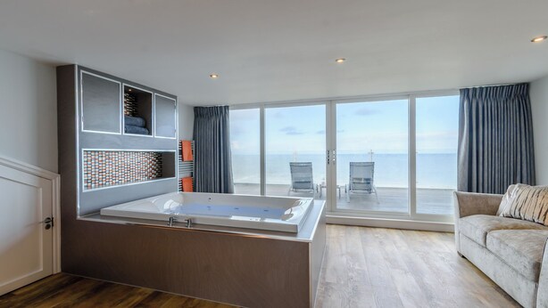 Une chambre moderne dotée d’une grande baignoire, d’un plancher en bois, d’un canapé et offrant une vue sur la mer grâce à de grandes fenêtres.