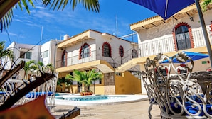 A courtyard with a pool, outdoor seating, and a building with balconies. - Bungalows Maria Teresa (Rincón de Guayabitos)