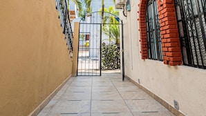 A narrow alleyway with tiled flooring, a gate, and a building with red brick arches and a white wall. - Bungalows Maria Teresa (Rincón de Guayabitos)