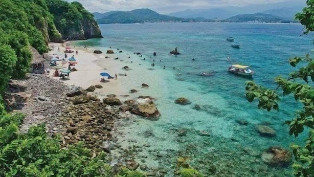 A beach with clear turquoise water, rocky shore, and lush greenery. - Bungalows Maria Teresa (Rincón de Guayabitos)