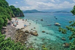 Une plage à l’eau turquoise et limpide, bordée d’un rivage rocheux et d’une végétation luxuriante.