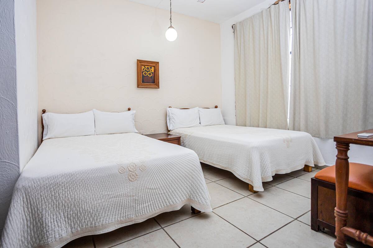 Habitación de hotel con dos camas, una mesita de noche de madera, una mesa y una lámpara colgante.