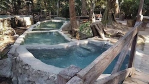 A naturalistic water feature with multiple pools surrounded by wooden structures and trees. - Bungalows Maria Teresa (Rincón de Guayabitos)