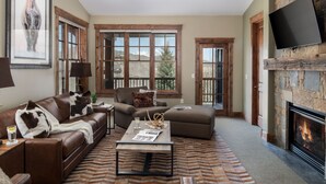 A living room with a fireplace, leather sofas, a coffee table, and large windows. - Outpost: Grand View 5230 - Incredible Teton Views! (Jackson)