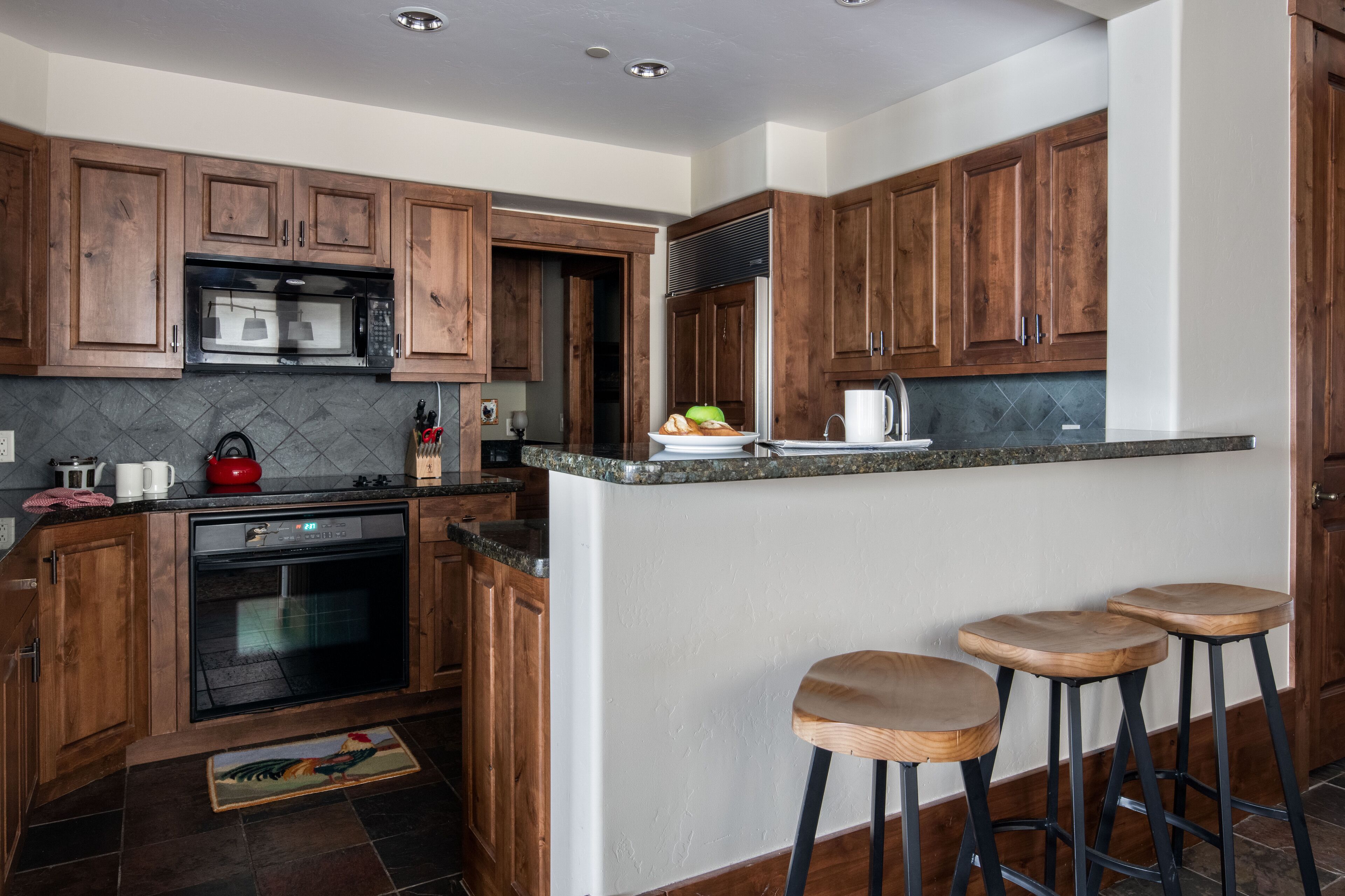 A kitchen with wooden cabinets, a microwave, an oven, a sink, and a bar area with stools.