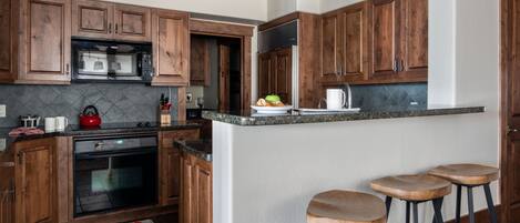 A kitchen with wooden cabinets, a microwave, an oven, a sink, and a bar area with stools.