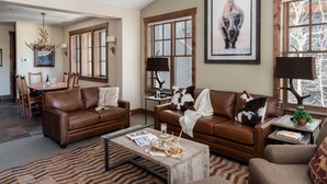 A spacious living room with a brown leather sofa, a wooden coffee table, and a dining area with a table and chairs. - Outpost: Grand View 5230 - Incredible Teton Views! (Jackson)