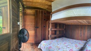 Una habitación tipo cabaña de madera con una cama, un ventilador y una ventana.