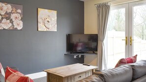 Ein Wohnzimmer mit einer Couch, einem Holztisch, einem Fernseher und zwei floralen Bildern an der Wand.