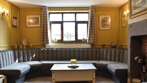 Ein gemütliches Zimmer mit einer großen, gebogenen Bank, einem zentralen Tisch und einem Kamin.