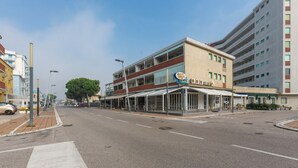 Un edificio a più piani con un bar-caffetteria al piano terra, una zona esterna coperta e un parcheggio.