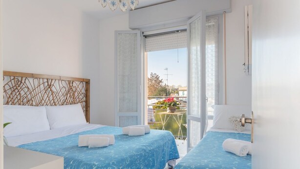 Una camera d'albergo con due letti, un balcone e vista esterna.