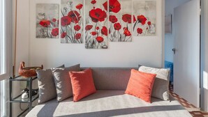 Un soggiorno con un divano grigio, cuscini rossi e grigi, e un quadro di papaveri appeso al muro.