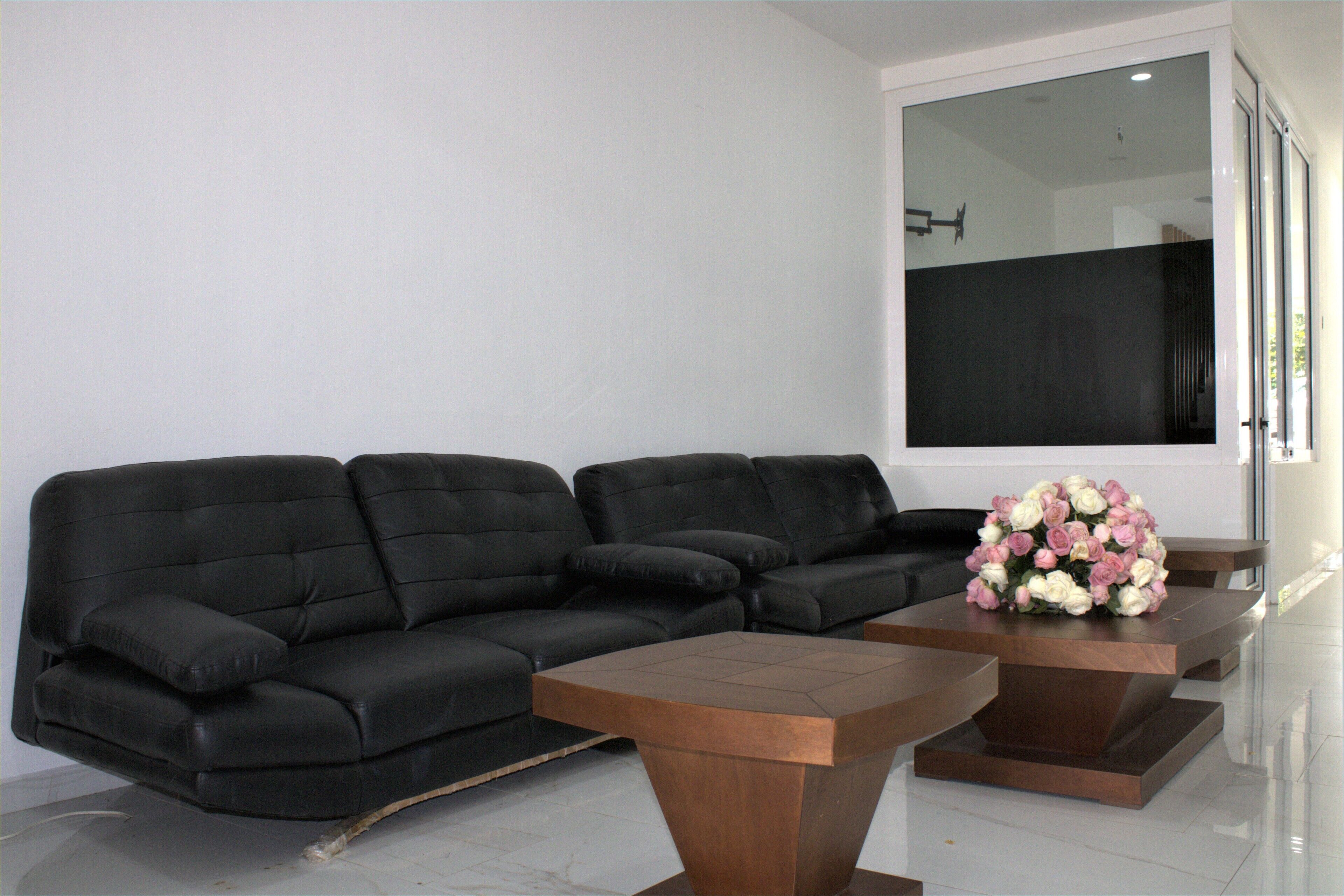 A modern living room with a black leather sofa, a wooden coffee table, and a bouquet of flowers.