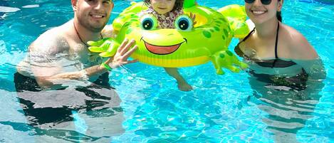 A pool with clear blue water, a green inflatable float, and people in the water.