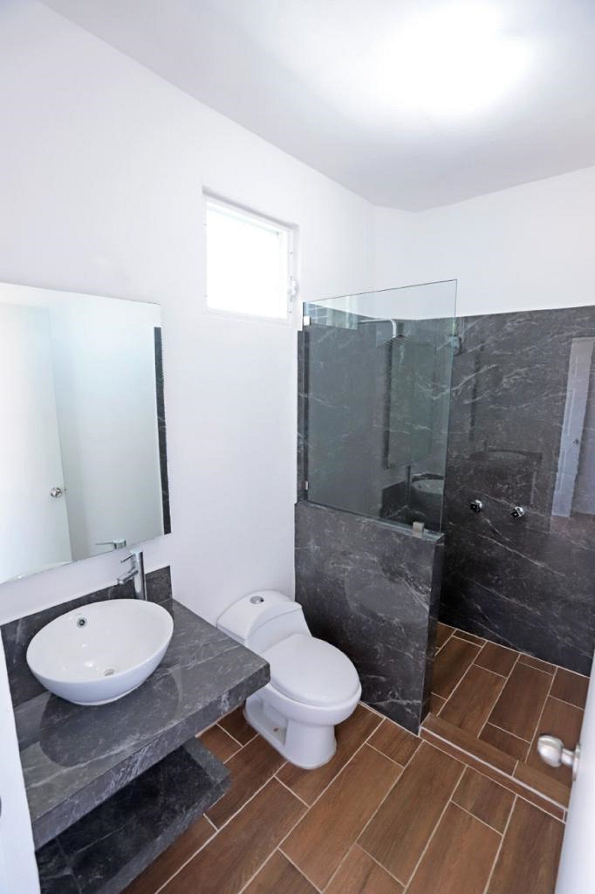 Un baño moderno con inodoro blanco, un espejo grande, lavabo blanco y cabina de ducha con paredes de vidrio.