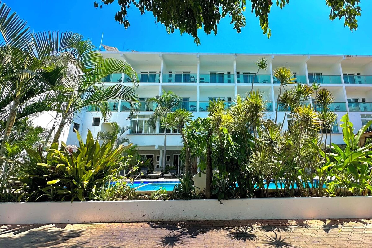 A multi-story hotel with a pool, surrounded by tropical plants.