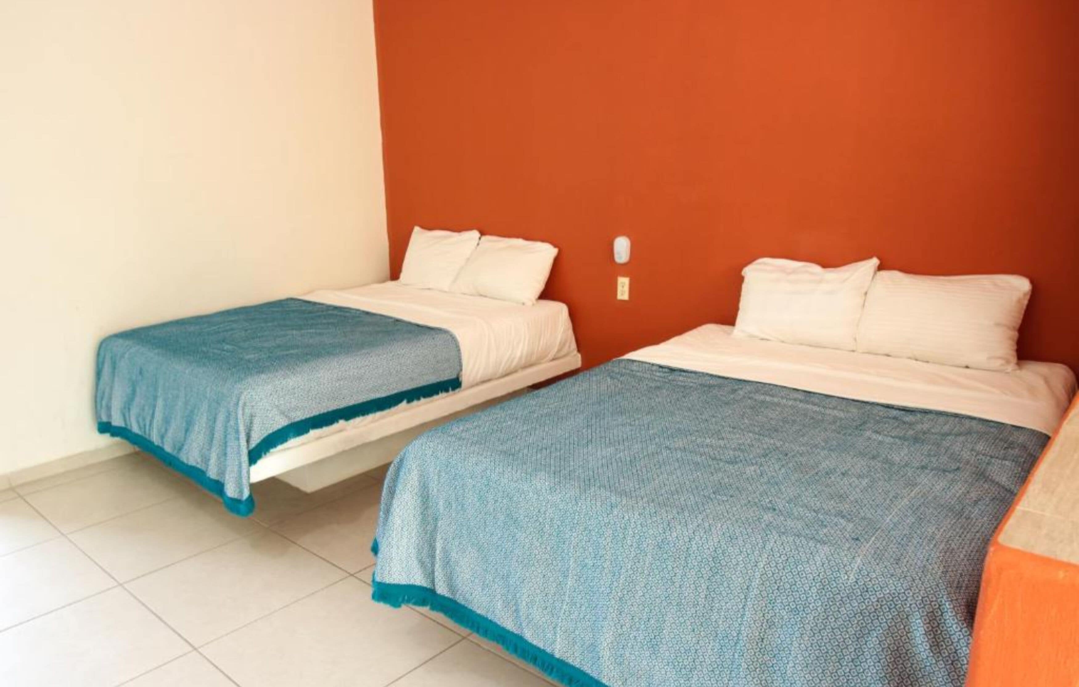 Dos camas individuales con ropa de cama azul y blanca en una habitación con paredes naranjas y suelo blanco.