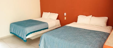 Dos camas individuales con ropa de cama azul y blanca en una habitación con paredes naranjas y suelo blanco.
