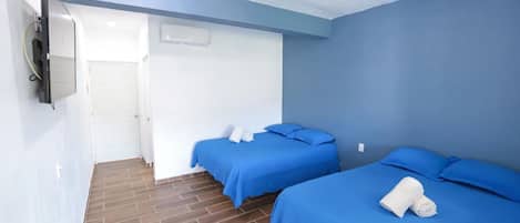 Una habitación con dos camas, un televisor montado en la pared y una puerta que da a otra habitación.