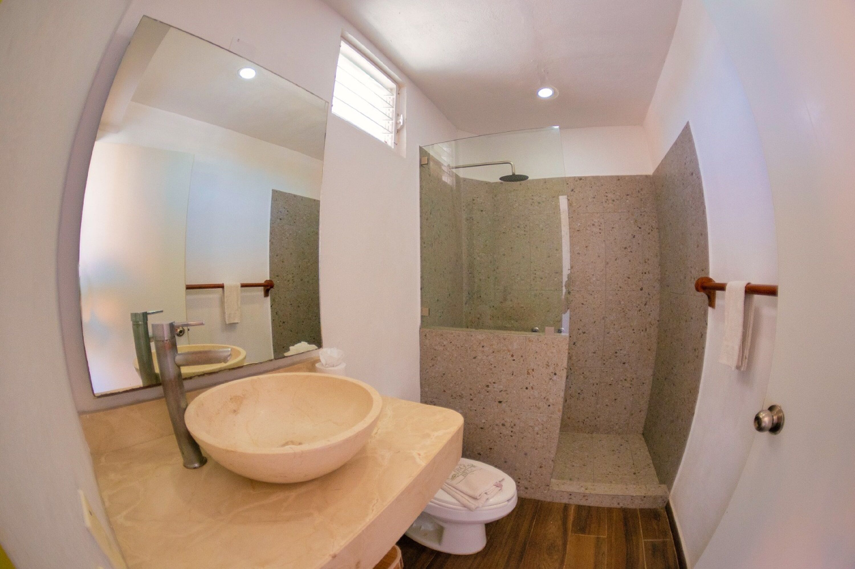 A bathroom with a large mirror, a bowl sink, a toilet, and a shower enclosure.