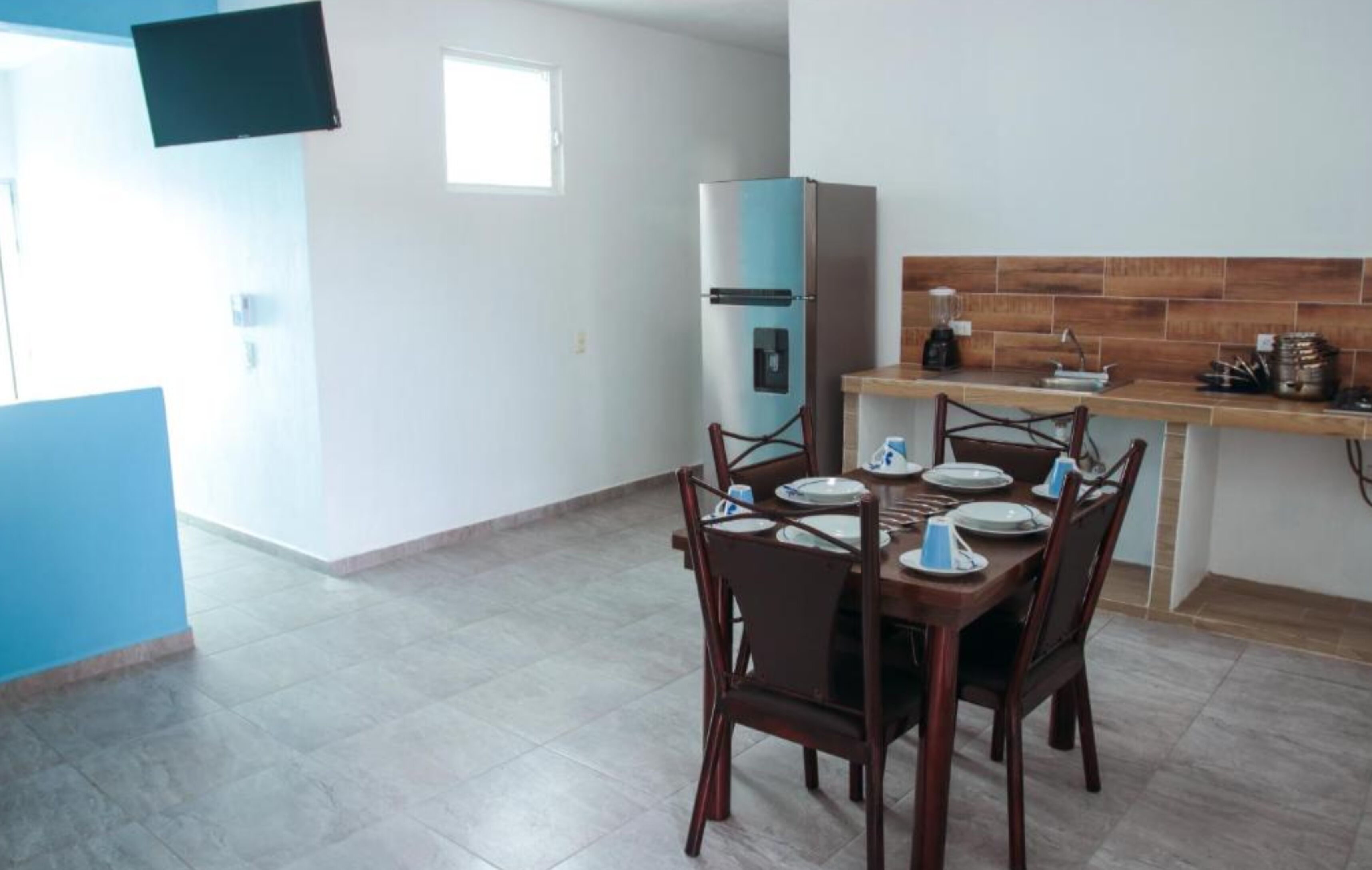 A compact kitchen with a dining area, a blue refrigerator, and a tiled backsplash.