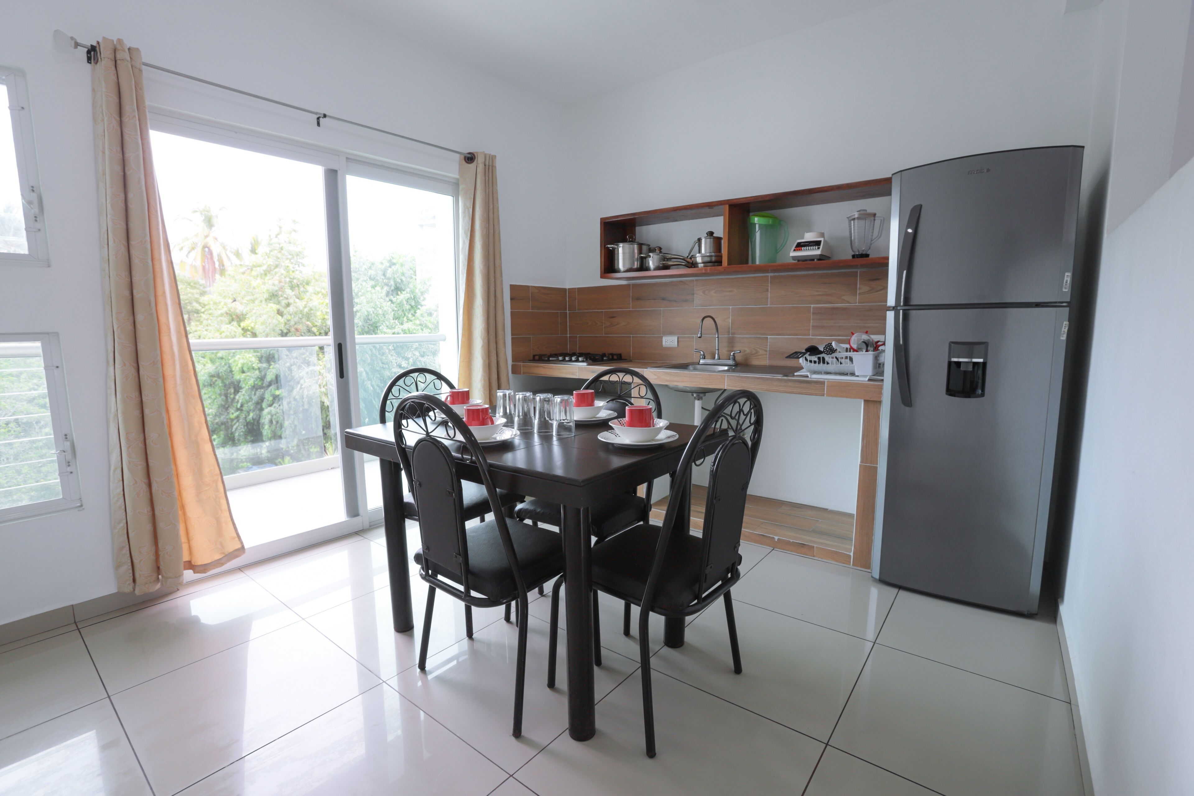 A modern kitchen with a dining table set for four, a built-in oven, and a refrigerator.