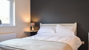 A neatly made bed with white linens, a bedside lamp, and a window with blinds. - One Dorchester Drive - UK32037 (Whitechapel, near Longridge)