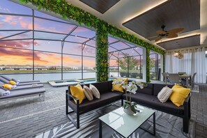 Un espacio lounge moderno al aire libre con piscina, sofá y mesa, destacando amplias ventanas y vistas a un cuerpo de agua.