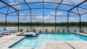 Relax by the tranquil pool, surrounded by lush greenery and a serene body of water.