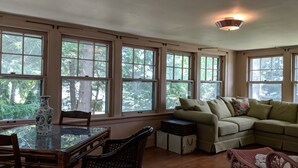 A spacious room with large windows, a dining table with chairs, a sofa, and a decorative vase.