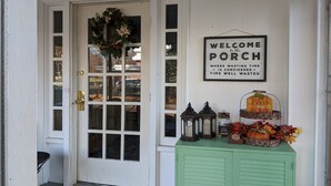 A white door with a glass panel and a wreath, a welcome sign, and a green cabinet with lanterns and a pumpkin decoration.