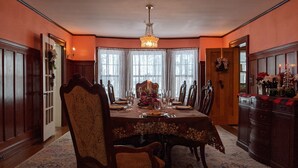 A formal dining room with a long table set for a meal, surrounded by ornate chairs, a chandelier, and a fireplace.