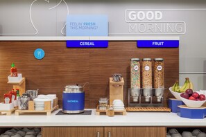 A breakfast bar with labeled sections for cereal and fruit, a ketchup dispenser, and a variety of condiments and utensils. - Holiday Inn Express Kermit By IHG (Kermit)