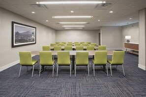 A conference room with a long table, green chairs, carpeted floor, and a framed picture on the wall. - Holiday Inn Express Kermit By IHG (Kermit)