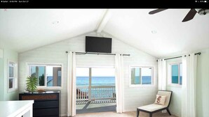 A bedroom with a balcony overlooking the ocean, a bed, a dresser, and a TV mounted on the wall. - Kahalu’u Surf and Snorkel Beachfront Paradise, with Hot Tub (Kailua-Kona)