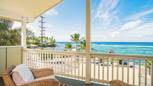 A balcony with wicker furniture, overlooking a beach and ocean. - Kahalu’u Surf and Snorkel Beachfront Paradise, with Hot Tub (Kailua-Kona)