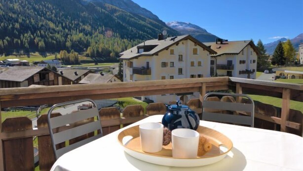 A table with a tray of cups and a teapot on a balcony overlooking a mountainous landscape.
