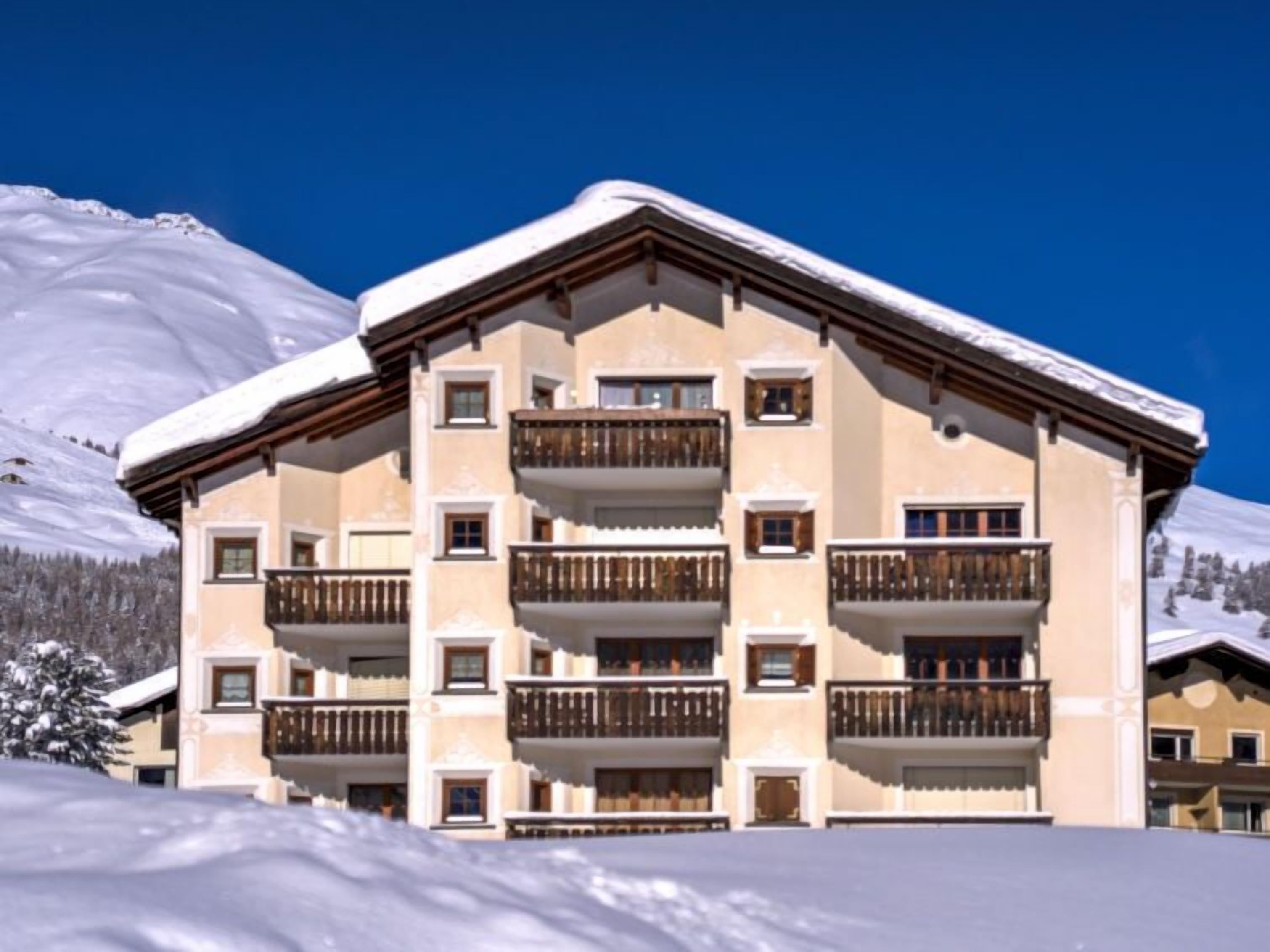 A multi-story building with balconies, set against a snowy mountain backdrop.