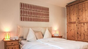 A bedroom with a large bed, two bedside tables with lamps, a wooden wardrobe, and a wall-mounted artwork.