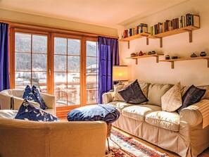 Ein gemütliches Wohnzimmer mit einer Couch, einem Sessel und Blick auf eine verschneite Landschaft durch große Fenster.