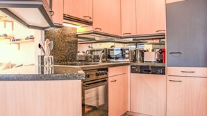 A modern kitchen with light wood cabinets, granite countertops, stainless steel appliances, and a built-in oven.