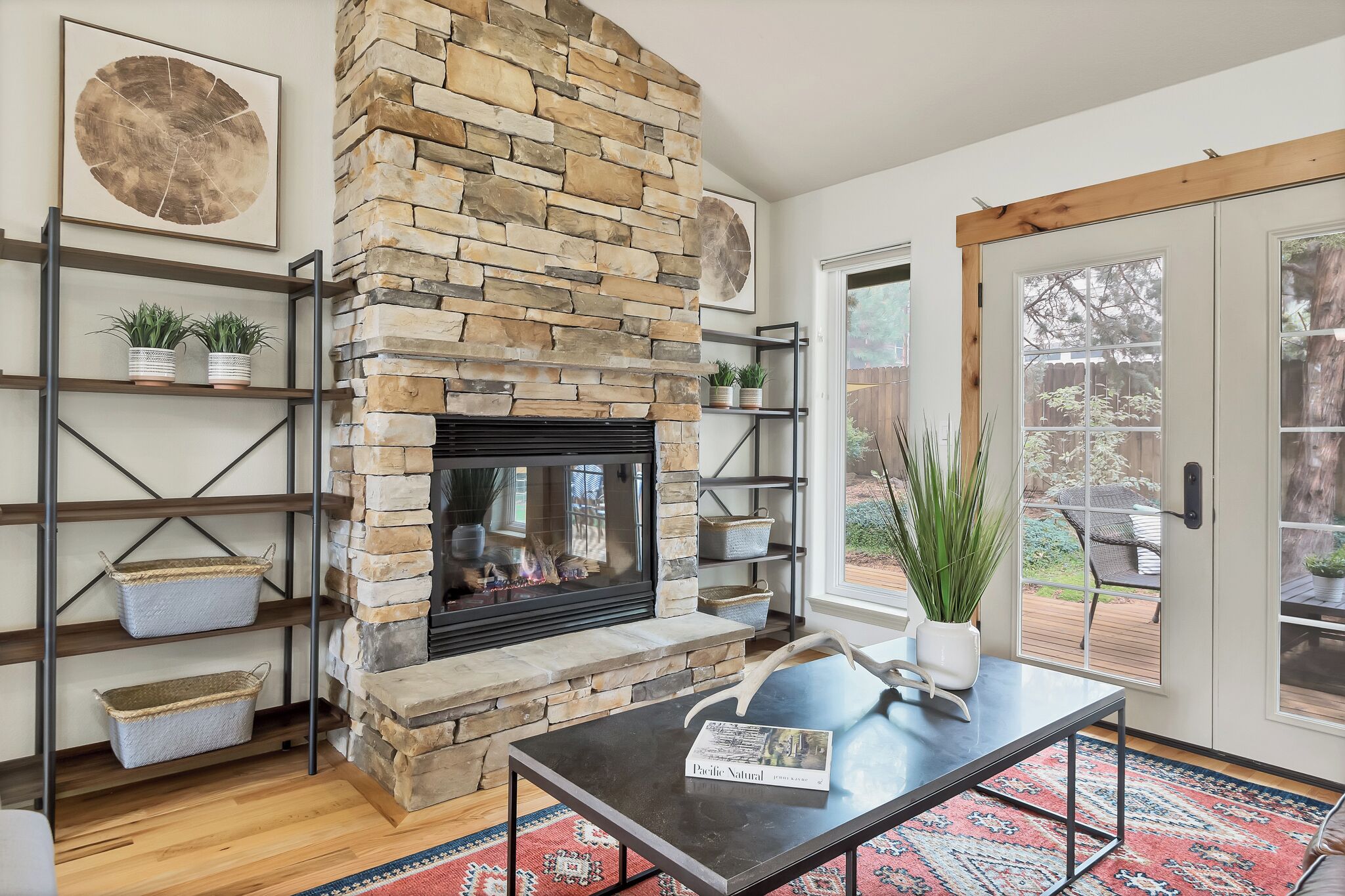 A living room with a stone fireplace, wooden shelves, and a glass door leading outside.
