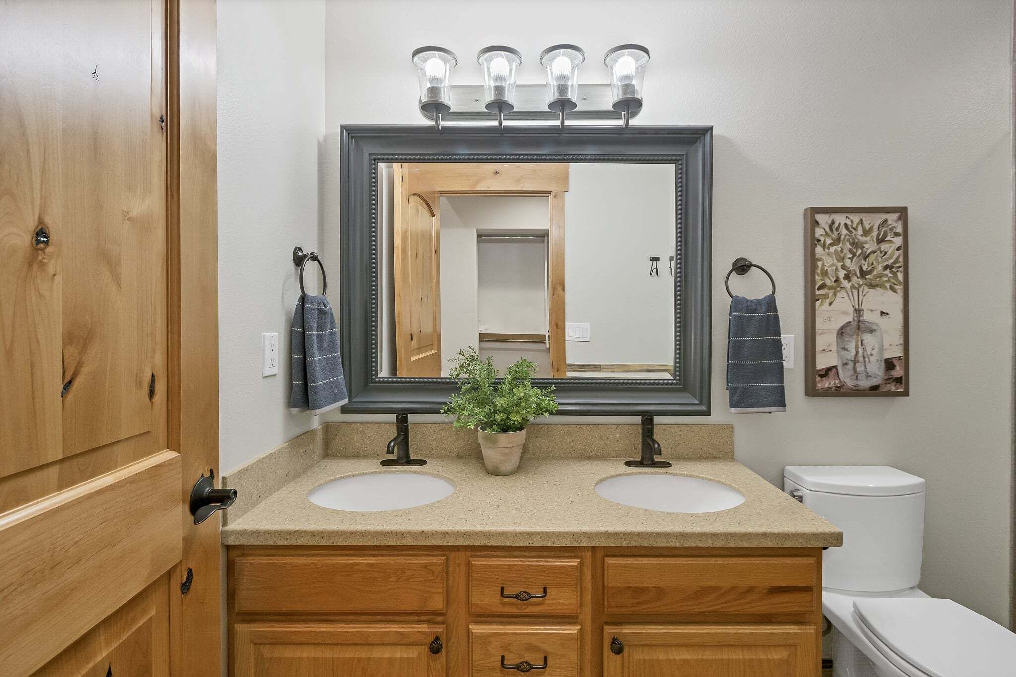 A bathroom with two sinks, a mirror, a potted plant, and a toilet.