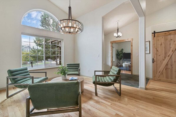 A spacious living area with a large window, a wooden floor, and a green upholstered chair.