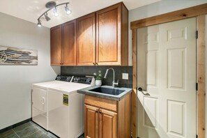 Cocina compacta con armarios de madera, lavadora, lavaplatos y una puerta con panel de vidrio.